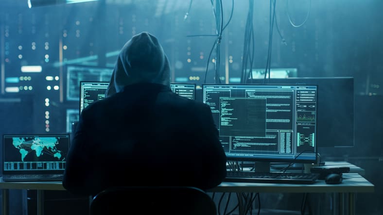 Dangerous Hooded Hacker Breaks into Government Data Servers and Infects Their System with a Virus. His Hideout Place has Dark Atmosphere, Multiple Displays, Cables Everywhere.